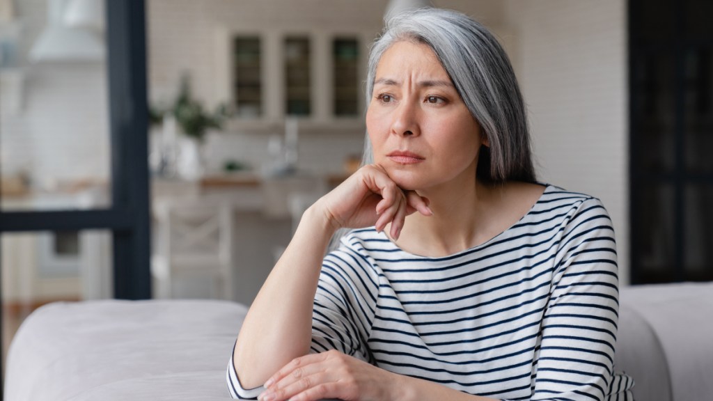 A woman with grey hair wearing a striped shirt who appears stressed and worried