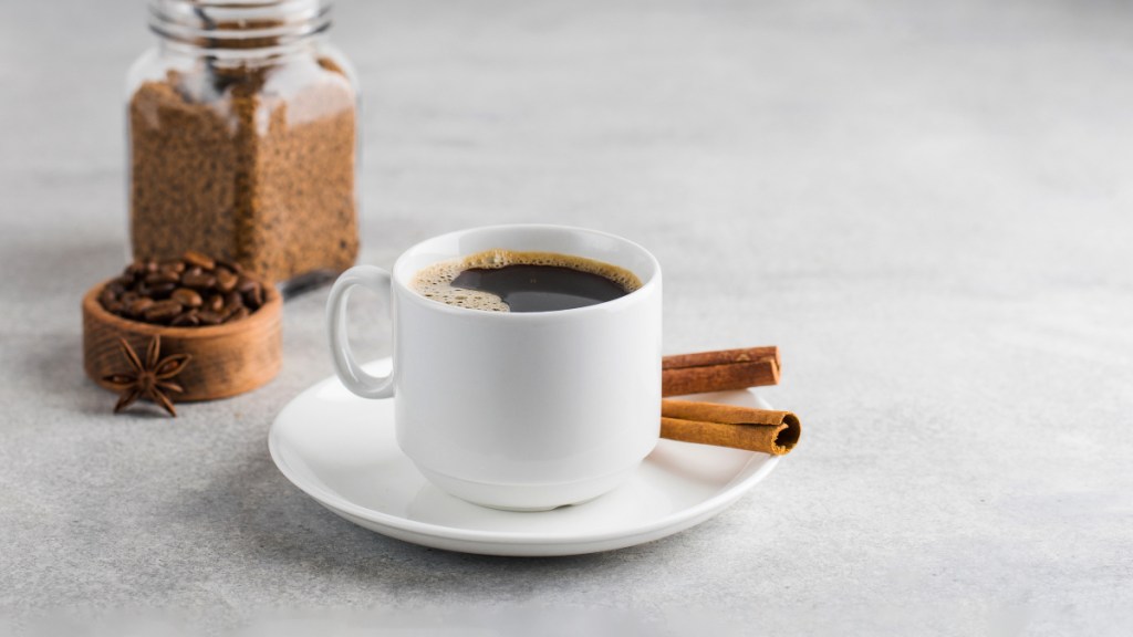 A cup of black coffee in a white mug beside fresh sticks of cinnamon