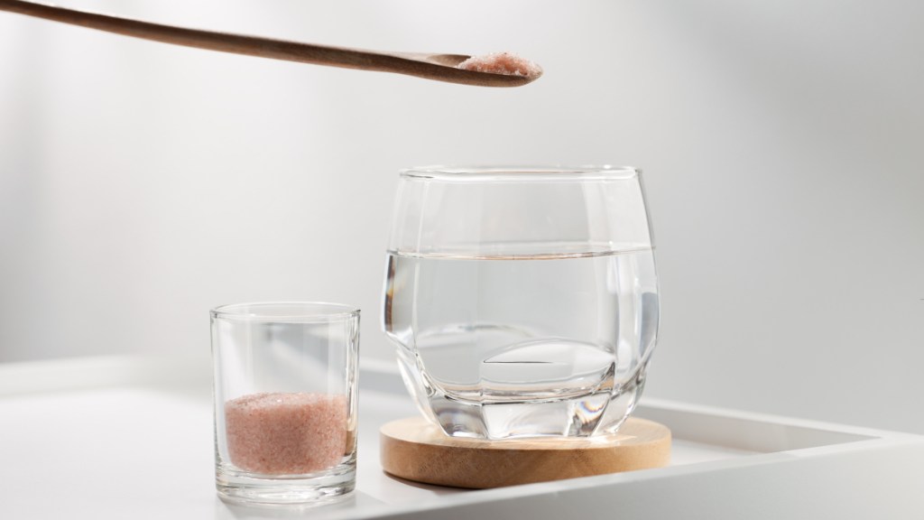 A glass of water beside pink Himalayan salt in wooden spoon for dehydration