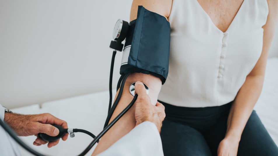 Close up of a woman in a white tank top getting her blood pressure read by a doctor