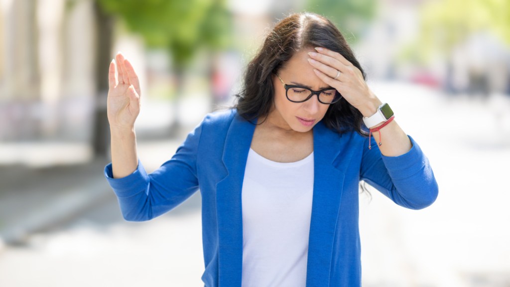 A woman in a blue shirt wearing glasses with her hand on her head due to dehydration