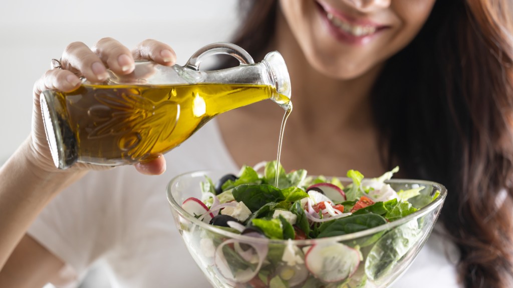 A woman pouring olive oil over a green salad to help ward off silent stroke symptoms