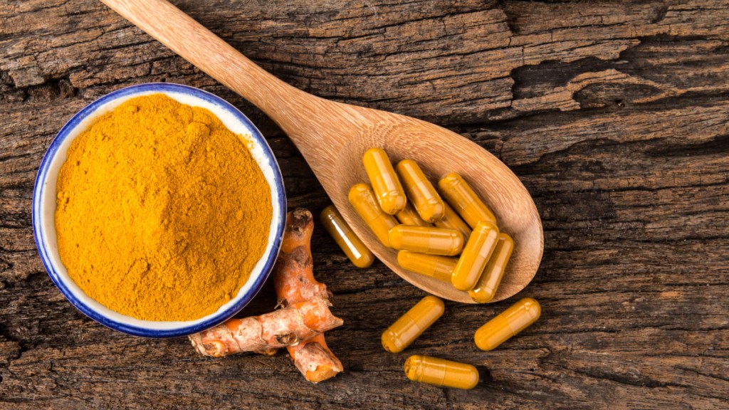 Turmeric powder in a bowl beside a spoon of curcumin pills, which ease hypertonic pelvic floor pain