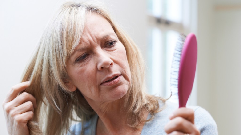 A blonde woman looking concerned while holding a pink hair brush