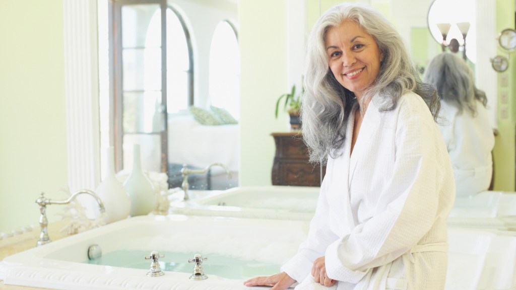 A woman with grey hair sitting on the edge of a tub filled with warm water