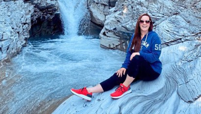 Gabrielle Carsala sitting by a waterfall, who found relief from chronic pain with infrared sauna blanket