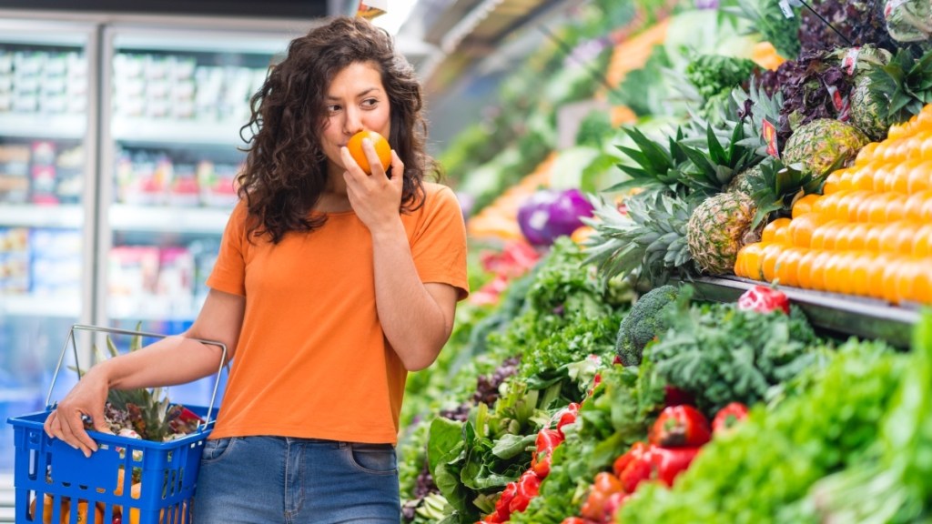 A woman with dark hair wearing an orange shirt shopping in a the produce aisle