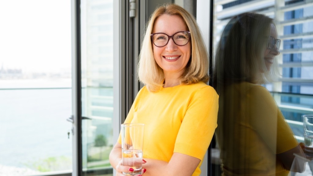 A woman in a yellow shirt with glasses hold a glass of water
