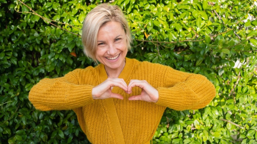 A woman in a gold sweater making a heart shape with her hands