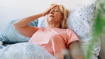 A woman lying in bed putting her hand on her head as she experiences hot flashes that are worse at night