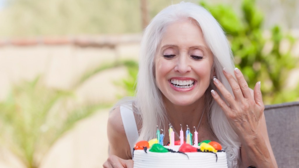 A woman with grey hair blowing out birthday candles who reversed her biological age