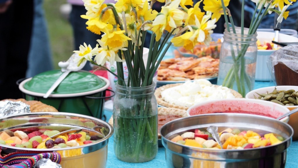 A table filled with healthy potluck dishes, like fresh fruit and green beans, and decorated with yellow daffodils
