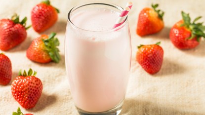 A glass of strawberry horchata (a rice-based chilled drink) on a table surrounded by fresh strawberries