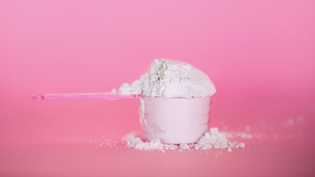 A measuring cup with creatine powder in it, which is beneficial for women, against a pink background