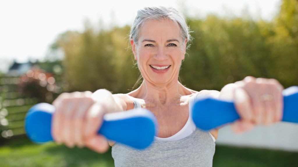 A mature woman lifting blue hand weights while smiling