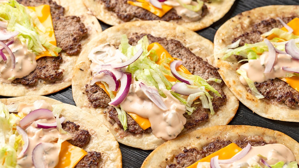 Several smash burger tacos on a dark serving board