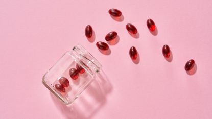 red astaxanthin pills emptied from jar against a pink background