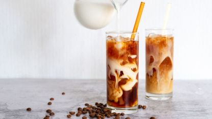 homemade cold brew in glass with straw against white background with cream poured in
