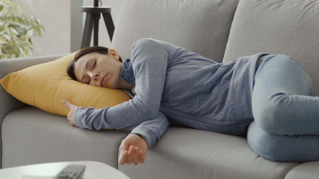 A woman napping on a grey couch with a yellow throw pillow